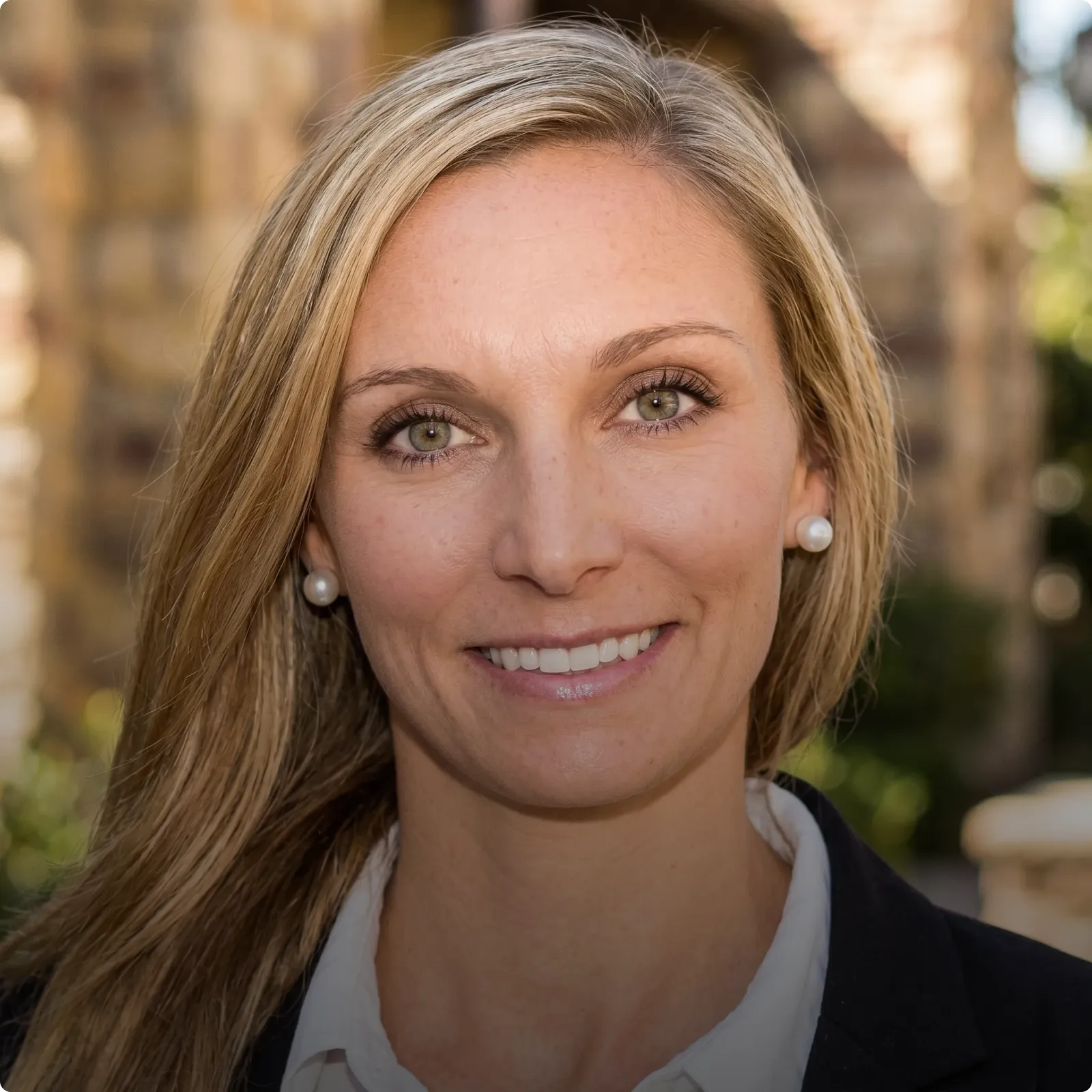 HOA attorney / HOA law A woman with long blonde hair and a professional smile, wearing a white shirt and a black blazer, in front of a blurred background.